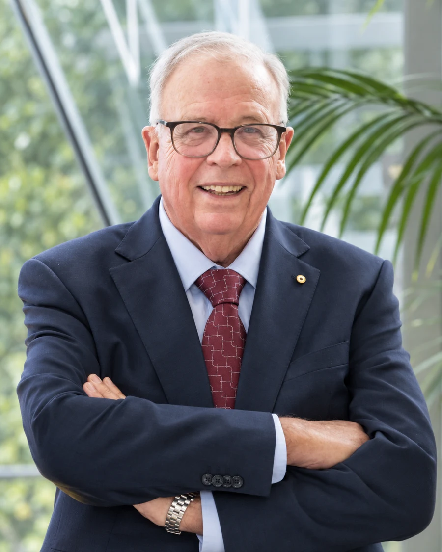 David Chandler AM smiling with his arms crossed, wearing a navy suit and glasses